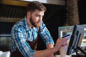 Handsome concentrated bearded waiter swiping credit card through the computer terminal in cafe-2